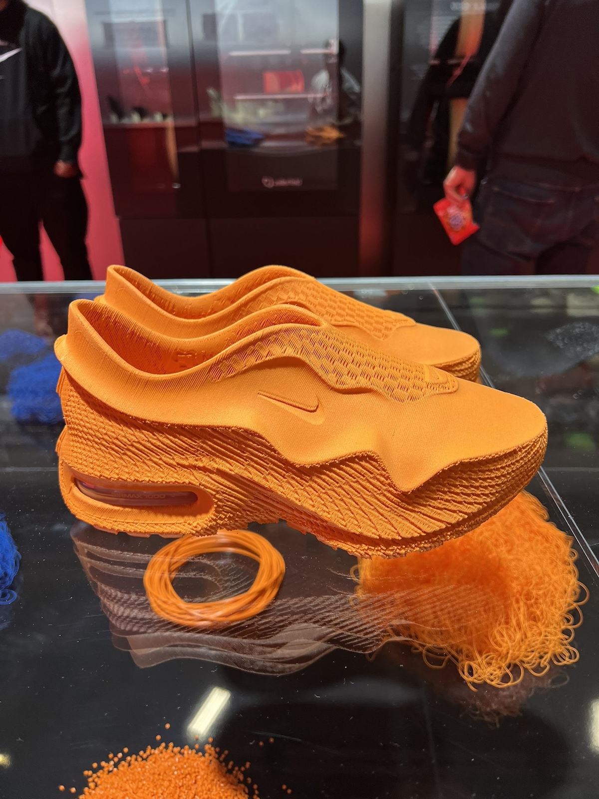 A close-up of the Nike Air Max 1000 in vibrant orange, highlighting the 3D-printed mesh upper and wavy sole unit for a futuristic look.