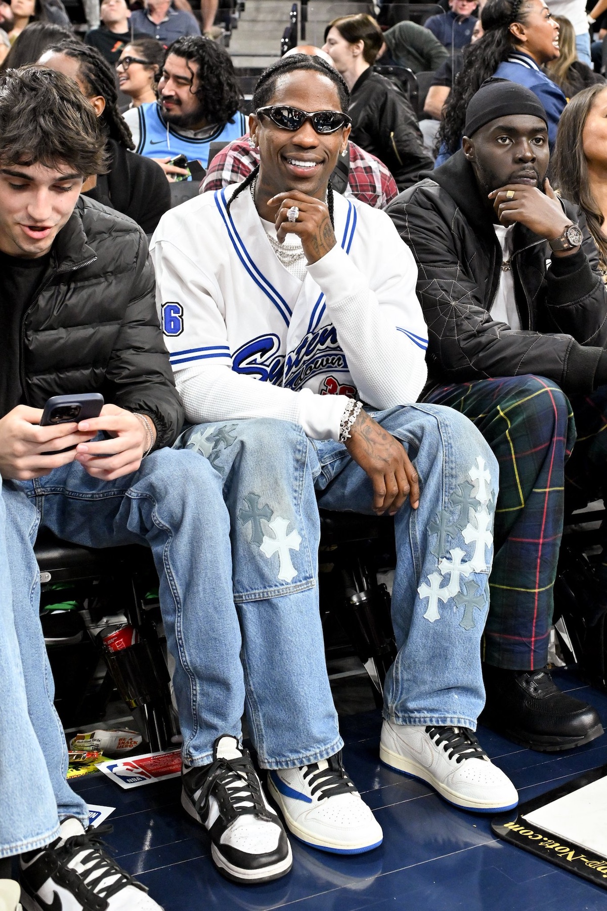 ravis Scott courtside wearing Air Jordan 1 Low OG Fragment, paired with Chrome Hearts jeans and vintage System baseball jersey.