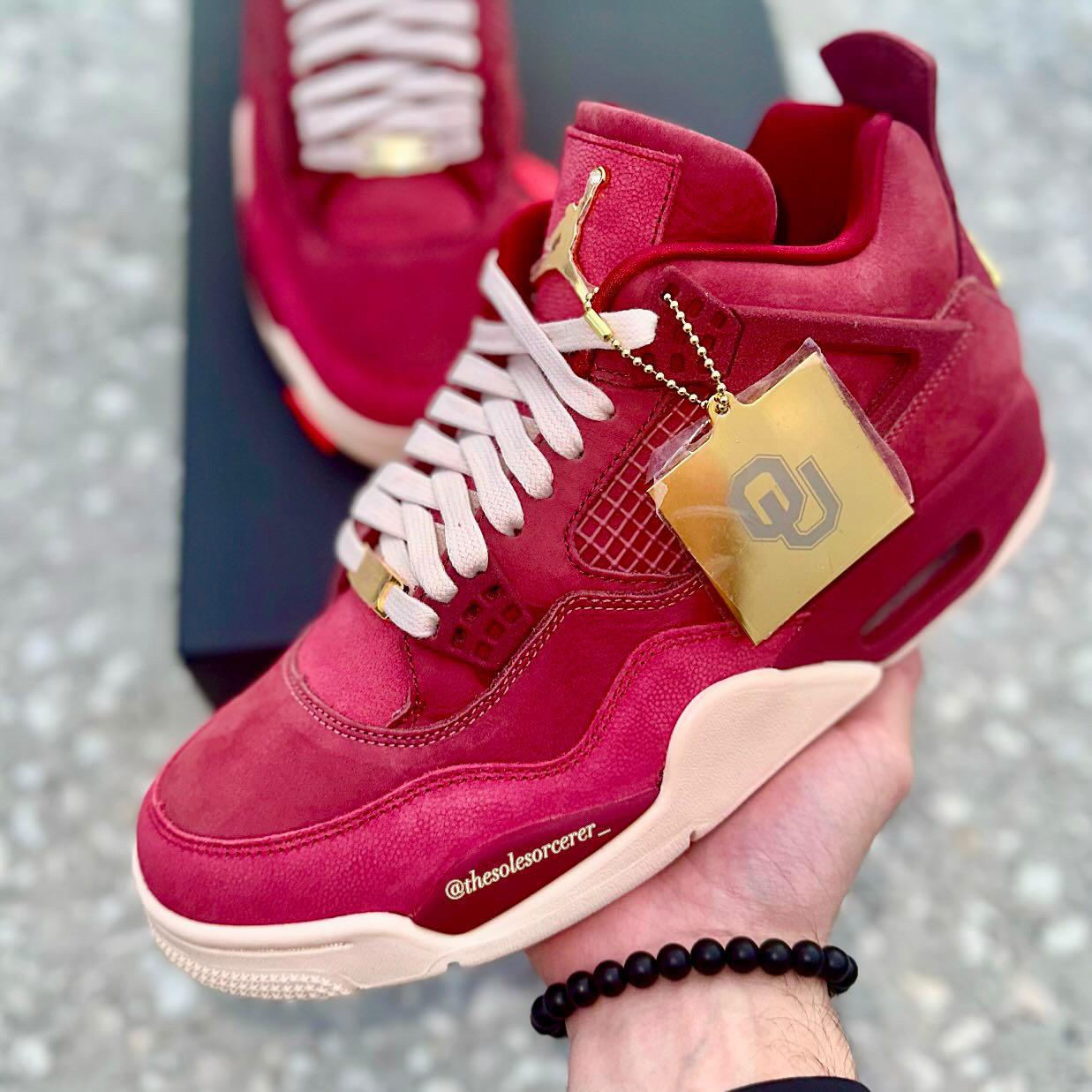 Air Jordan 4 Oklahoma Sooners PE held in hand showcasing crimson suede and gold accents