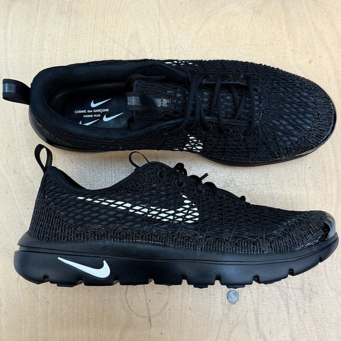 Side-by-side of black and white CDG x Nike Air Rejuven8 pairs on display.