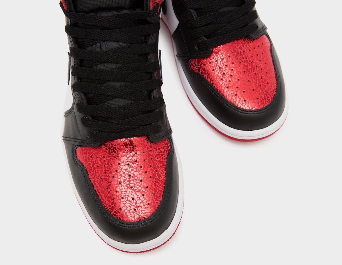 Overhead view of the Air Jordan 1 High OG's toe box, featuring vibrant cracked red leather with perforations for breathability. Black leather overlays frame the toe area, leading into the black laces and white midsole with a red outsole underneath.