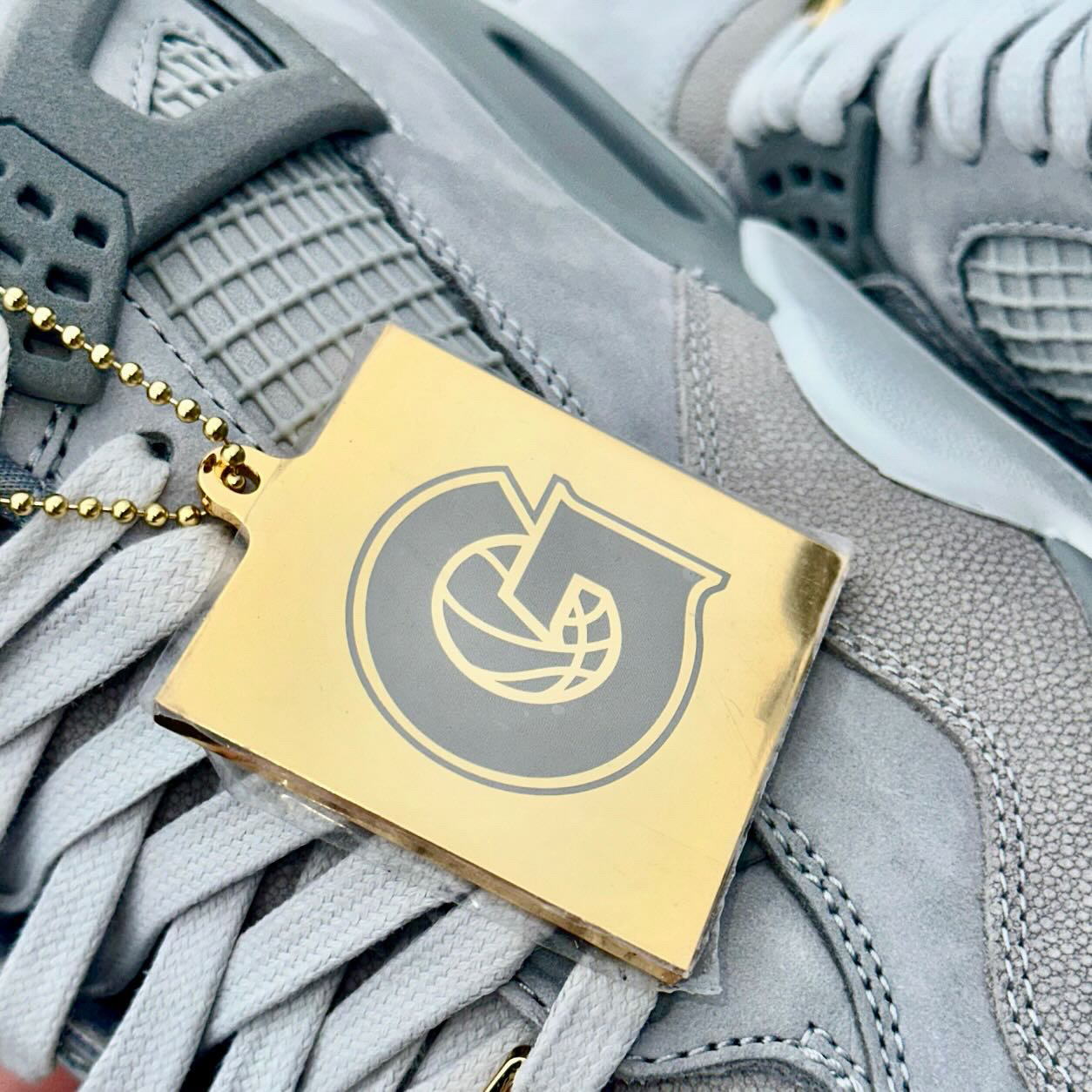 Close-up of the gold Georgetown Hoyas hangtag featuring the iconic "G" logo with a basketball graphic, attached to the Air Jordan 4 Georgetown PE.