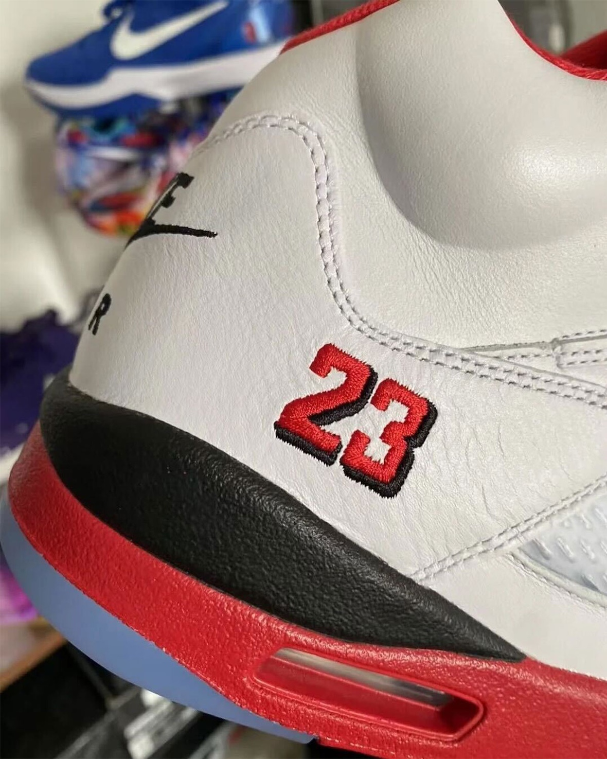 Side view of the Air Jordan 5 Fire Red Black Tongue 2025, featuring the embroidered red and black "23" branding on the lateral heel, black and red midsole, and translucent outsole.