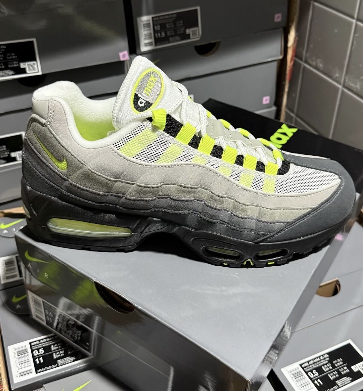 A first look at the next 2025 Nike Air Max 95 OG 'Neon' with gradient gray -wild leather plates, neon yellow top loops, black midsole and visible air units. The sneaker is displayed on its original packaging at the top, which highlights its classic retro design.