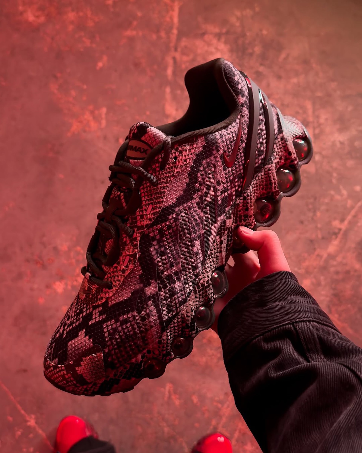 Nike Air Max Dn8 Snakeskin held under red light, showcasing faux snakeskin upper and Dynamic Air sole.