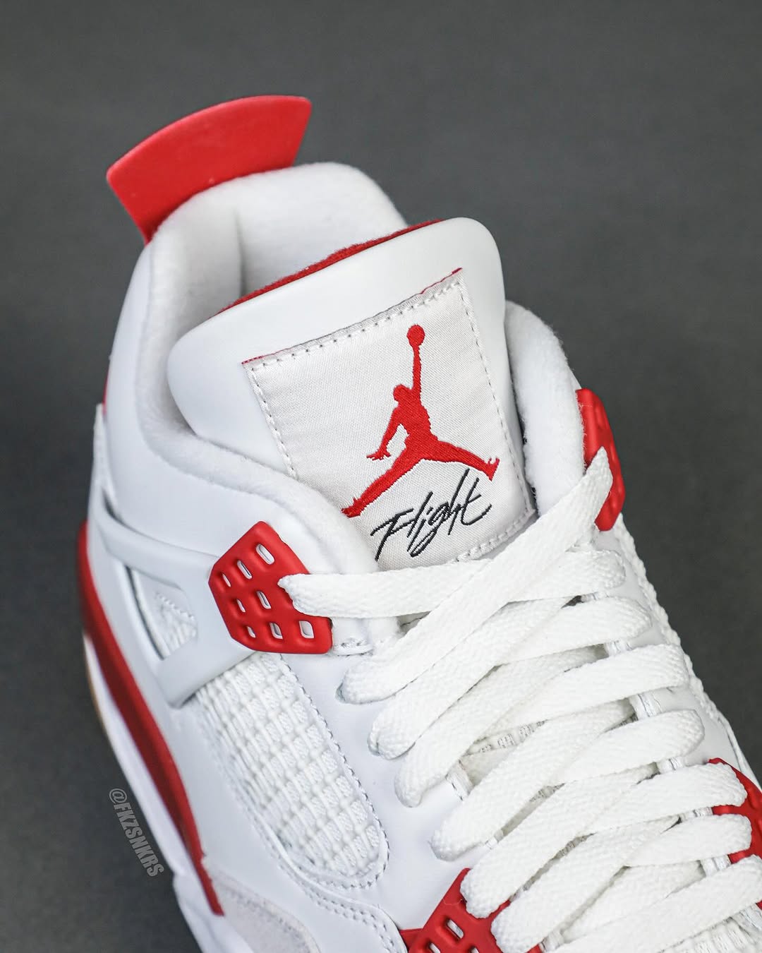 A close-up of the tongue on the Nike SB x Air Jordan 4 'Varsity Red' Friends & Family, featuring the Jumpman Flight logo in red embroidery on a white tongue.