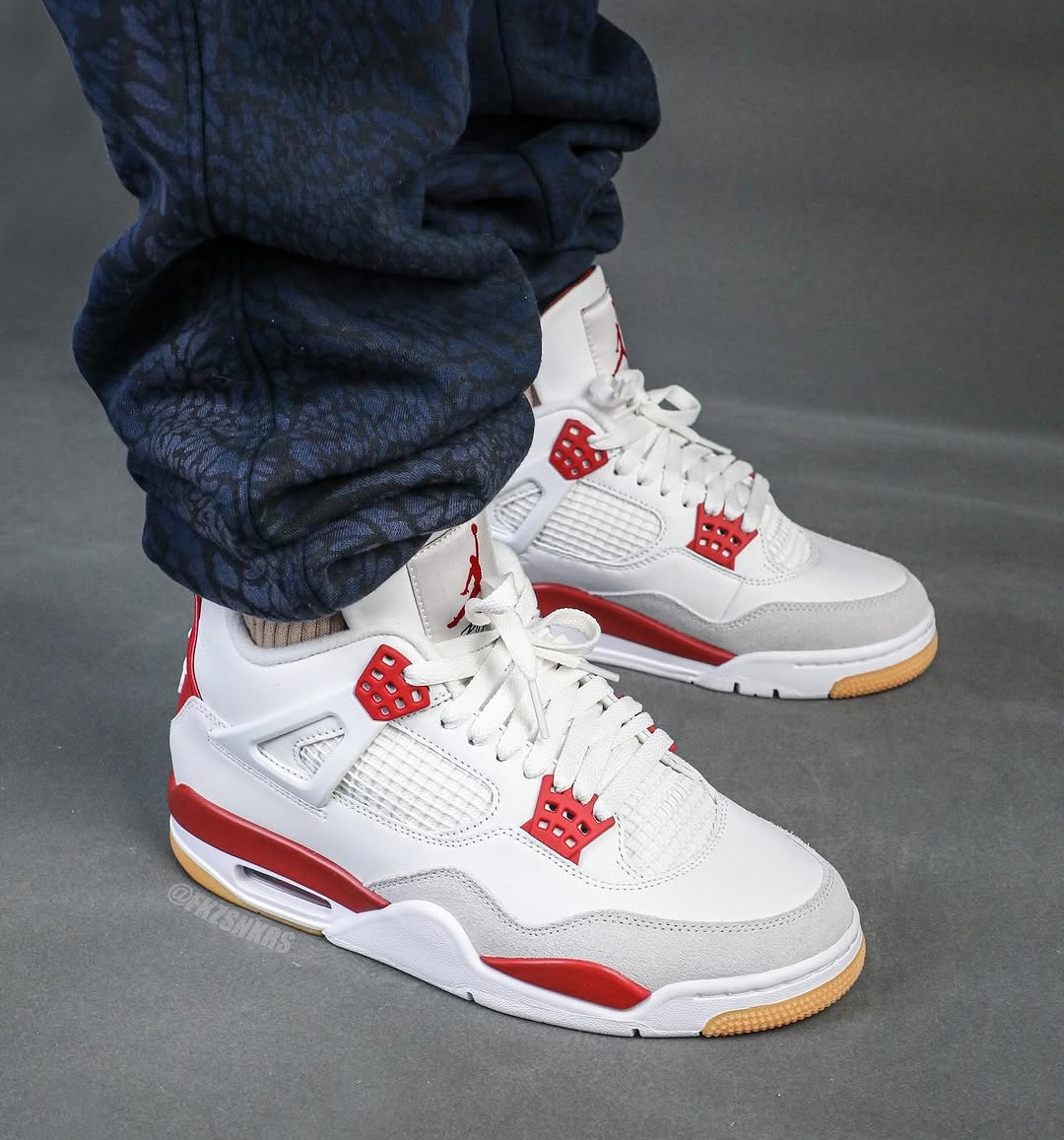 An on-foot look at the exclusive Nike SB x Air Jordan 4 'Varsity Red' Friends & Family edition, featuring a white leather upper with red and grey accents and a gum outsole.