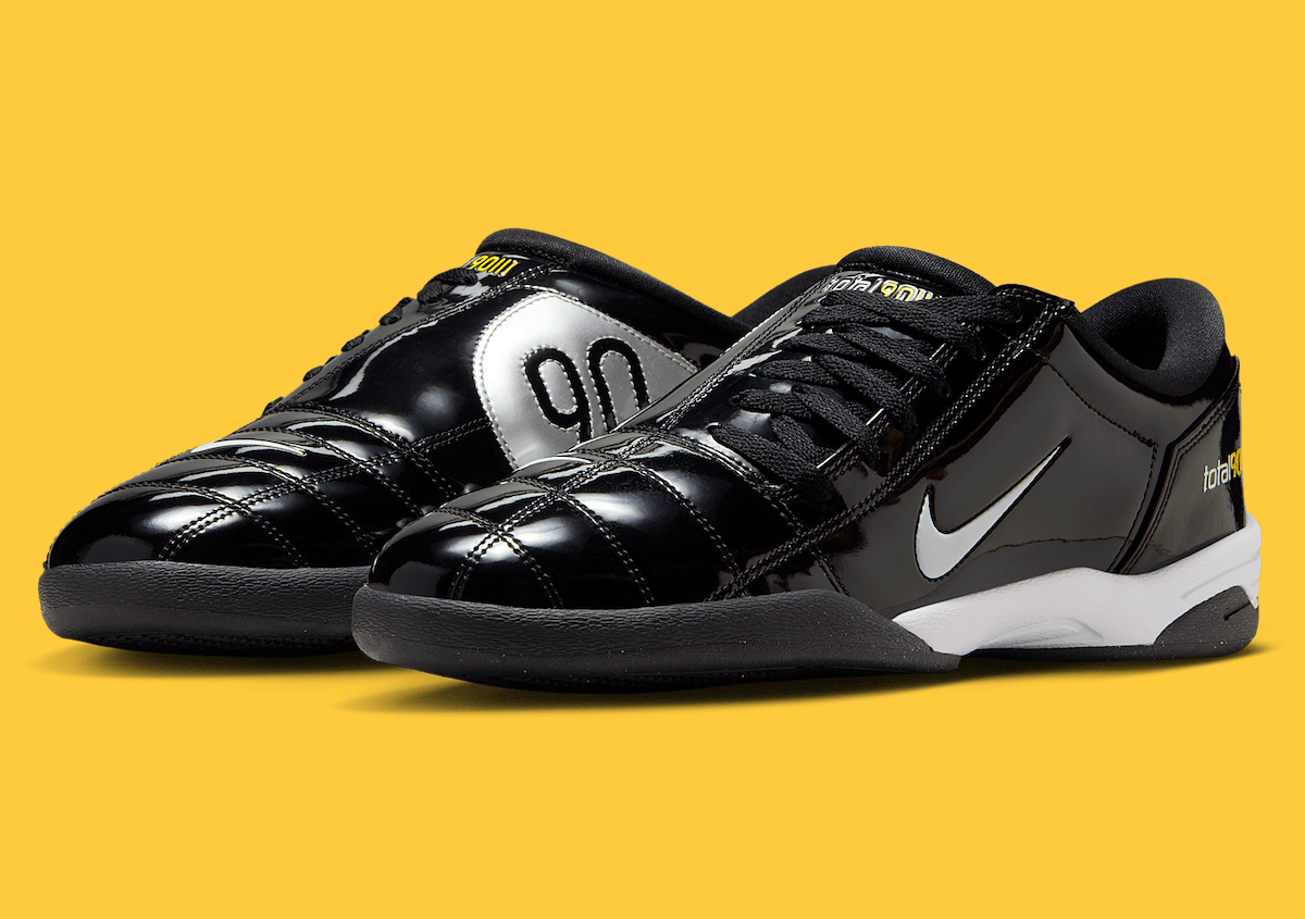 A pair of Nike Total 90 III Black Patent sneakers displayed against a yellow background, showcasing their glossy patent leather upper, silver branding, and yellow accents.