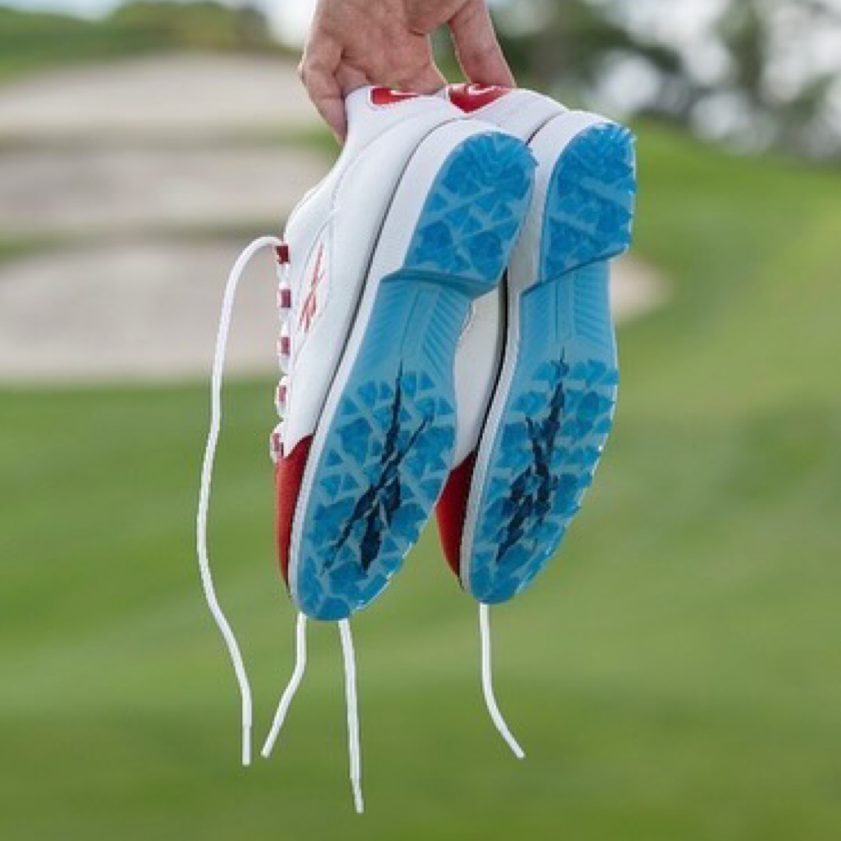 A golfer holding the Reebok Question Low Golf sneakers, showing the translucent sole.