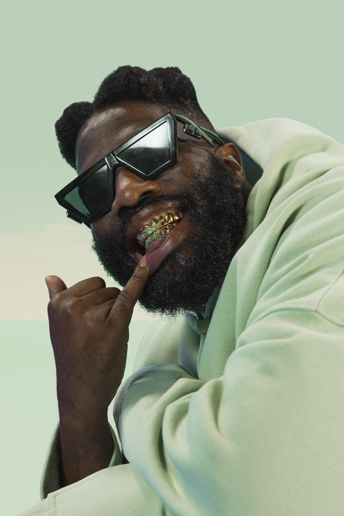 Close-up of Tobe Nwigwe wearing oversized sunglasses, showing his gold grill with Mint Green detailing