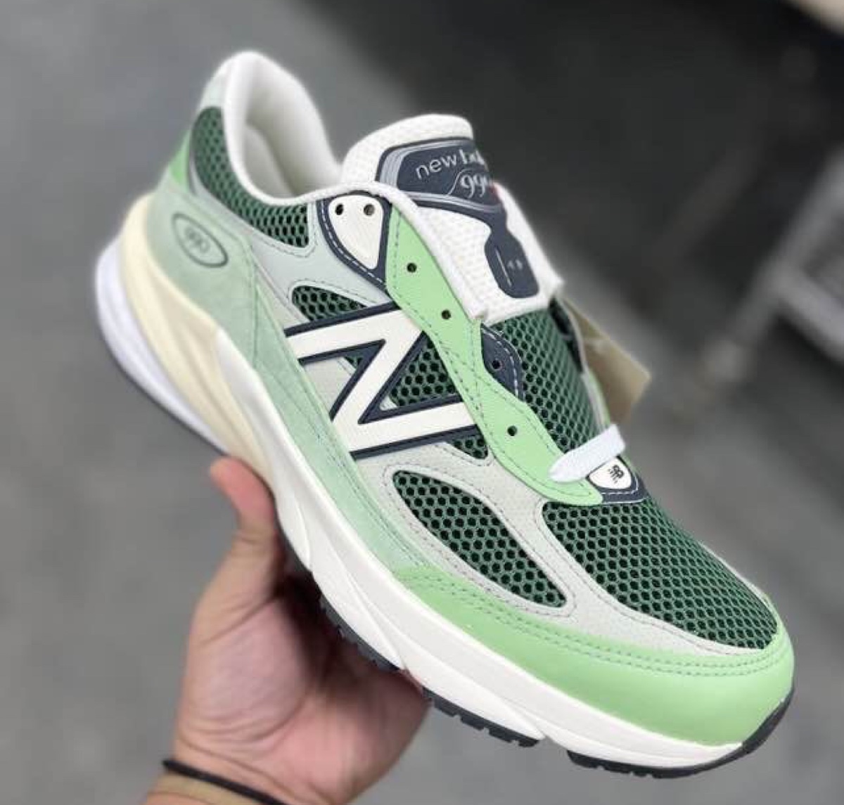 New Balance 990v6 Avocado Natural Mint sneaker in hand, showcasing its fresh green suede and mesh upper.