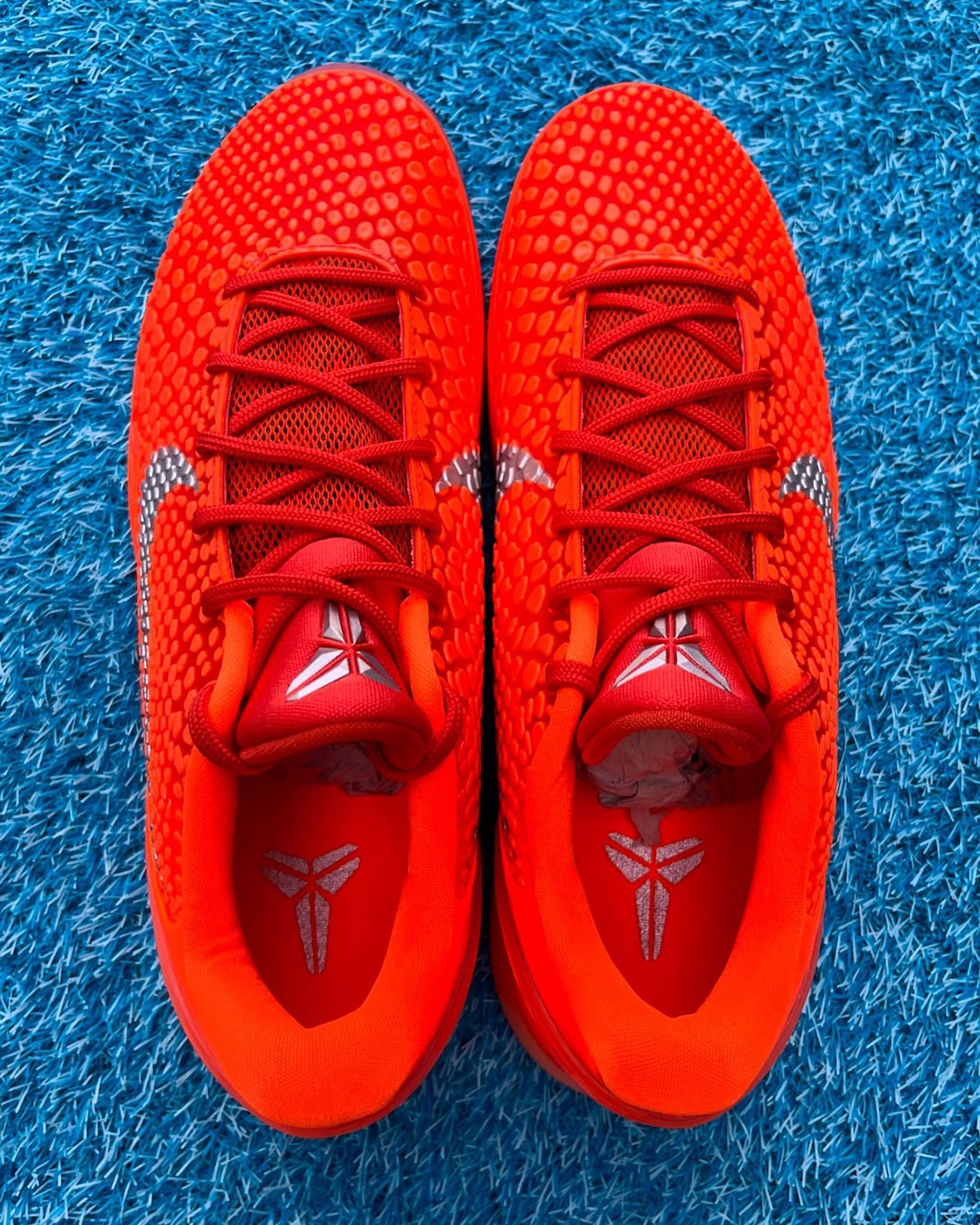 A top-down view of the Nike Kobe 6 Protro "Total Orange" showcasing the scaly-textured upper, red laces, silver Kobe branding on the tongue, and insole details against a bright blue textured surface.
