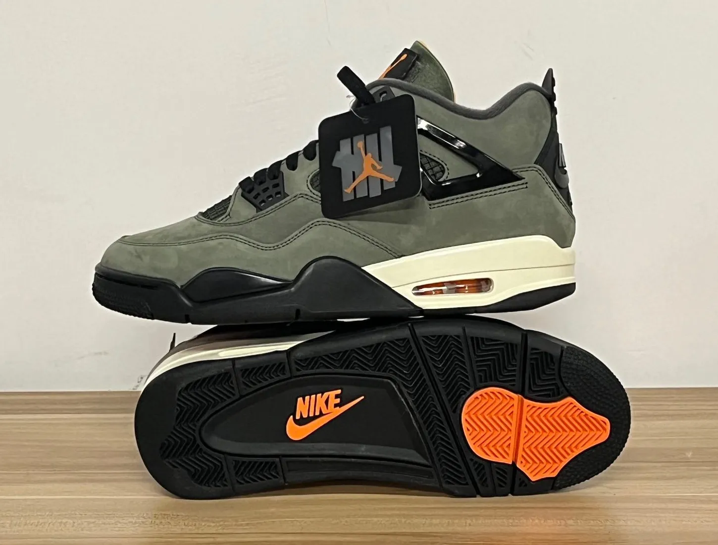 Undefeated x Air Jordan 4 2025 in Deep Green stacked to show outsole with orange Nike logo and black tread.