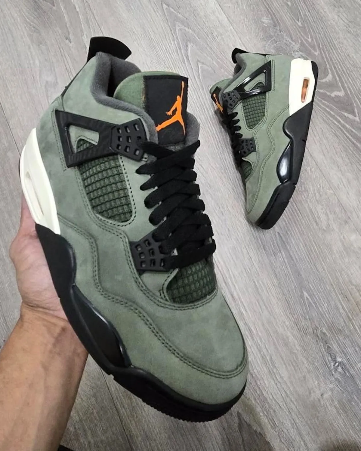 Undefeated Air Jordan 4 2025 sneaker in-hand view showing olive green suede upper and orange Jumpman logo