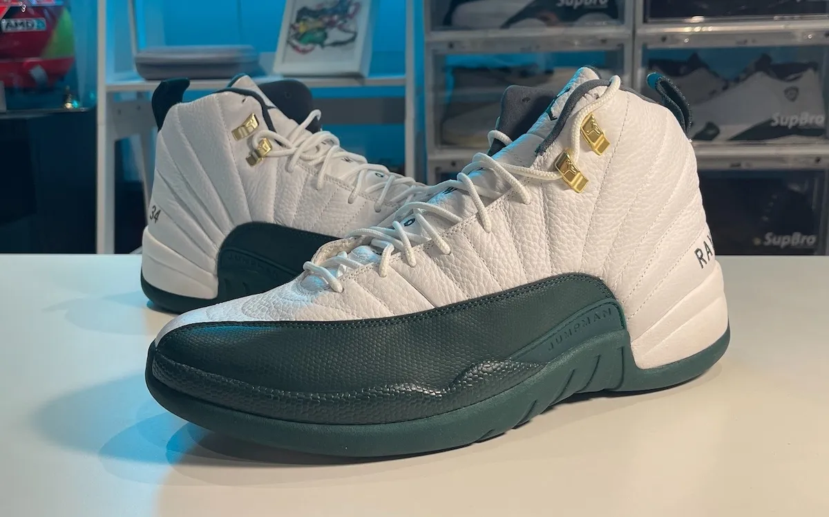 Close-up of the Air Jordan 12 “Bucks” PE, featuring a white leather upper with dark green overlays, gold eyelets, and Ray Allen’s 34 and RAY stitched details.